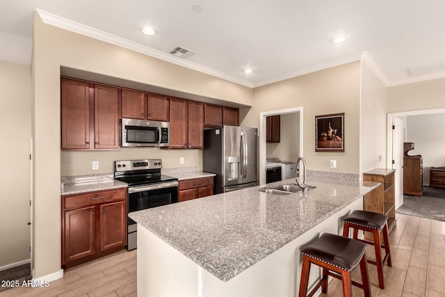 kitchen with light stone countertops, appliances with stainless steel finishes, sink, ornamental molding, and a breakfast bar area