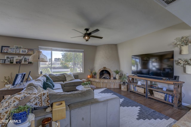 living room with ceiling fan, a large fireplace, and dark wood-type flooring