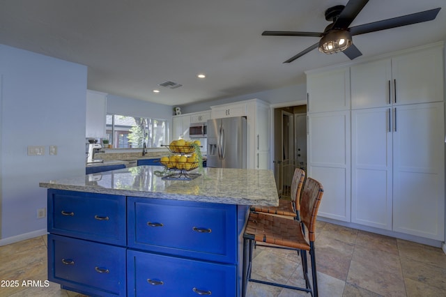 kitchen featuring a center island, white cabinets, light stone countertops, blue cabinetry, and stainless steel appliances