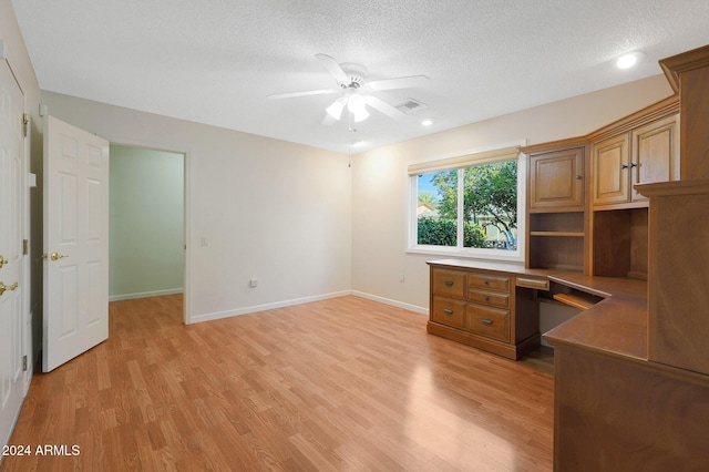 unfurnished office with a textured ceiling, light hardwood / wood-style floors, ceiling fan, and built in desk