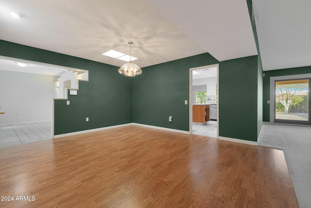 unfurnished room with a textured ceiling, light hardwood / wood-style floors, an inviting chandelier, and a wealth of natural light