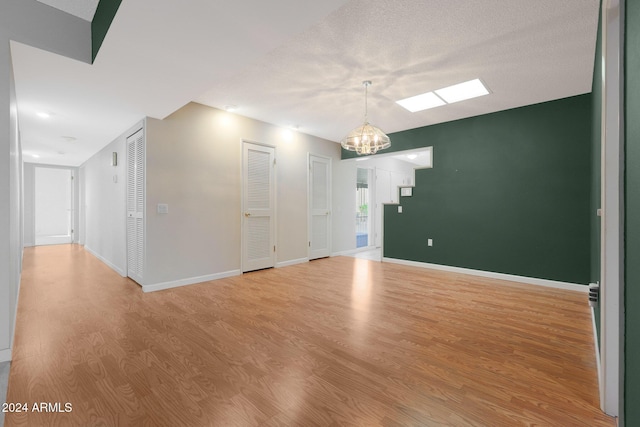 unfurnished room with a textured ceiling, an inviting chandelier, and light hardwood / wood-style flooring