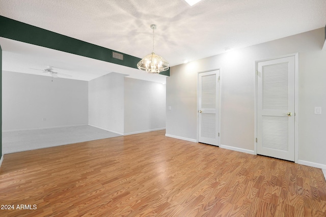 unfurnished room featuring a textured ceiling, ceiling fan with notable chandelier, and light hardwood / wood-style floors