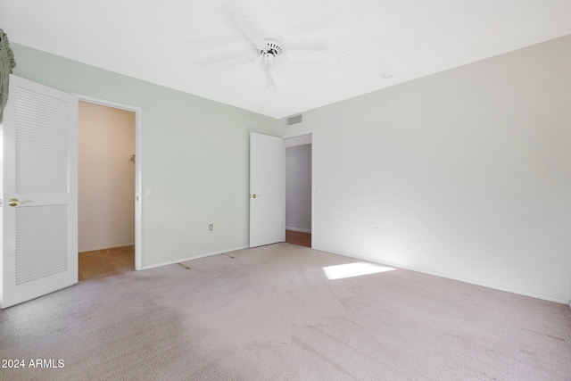 unfurnished bedroom with a walk in closet, ceiling fan, a closet, and light colored carpet