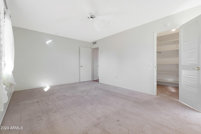 unfurnished bedroom featuring ceiling fan, a spacious closet, light carpet, and a closet