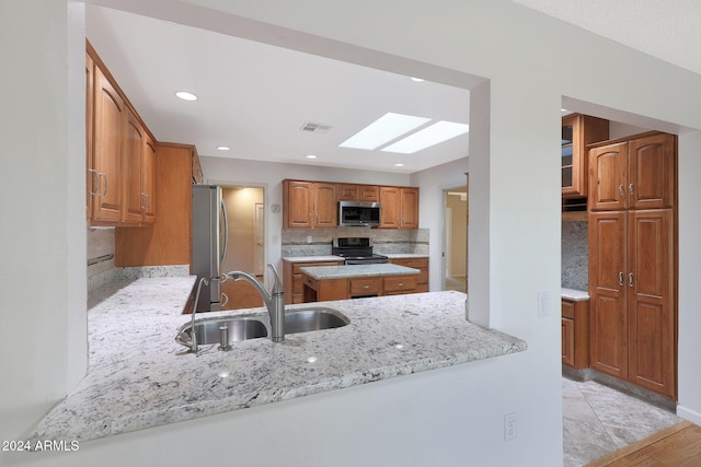 kitchen with a skylight, sink, stainless steel appliances, backsplash, and kitchen peninsula