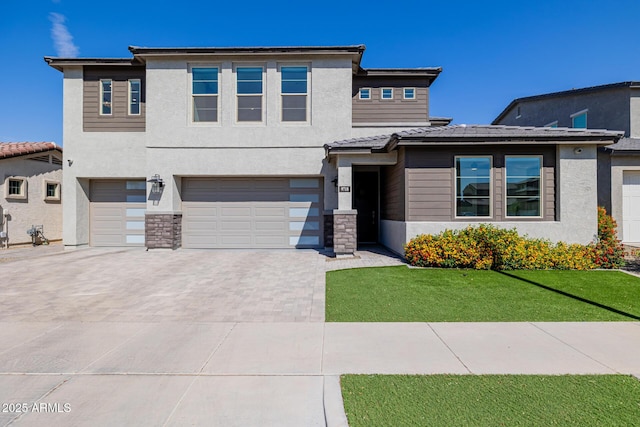 prairie-style house with stucco siding, driveway, stone siding, a front yard, and a garage