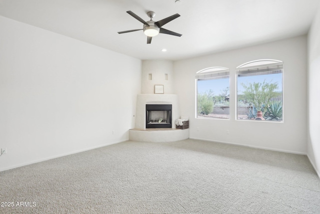 unfurnished living room with baseboards, a large fireplace, a ceiling fan, and carpet floors