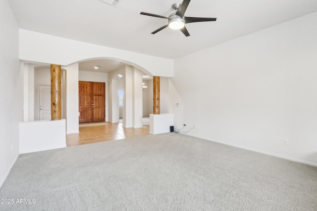 interior space with light tile patterned floors, baseboards, arched walkways, ceiling fan, and light carpet