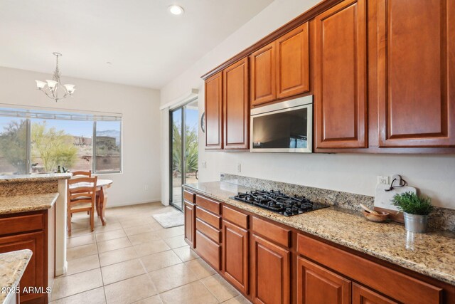 kitchen featuring stainless steel microwave, light stone counters, a notable chandelier, and black gas stovetop