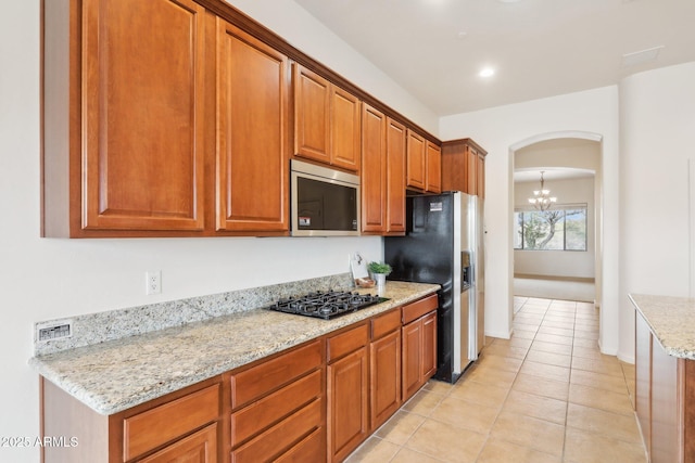 kitchen with brown cabinetry, light stone countertops, light tile patterned flooring, arched walkways, and stainless steel appliances