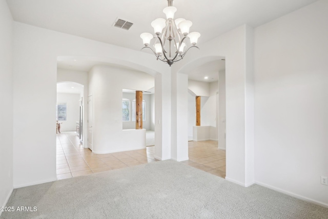 spare room featuring visible vents, light tile patterned floors, light colored carpet, and arched walkways