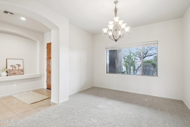 carpeted spare room with tile patterned flooring, visible vents, baseboards, an inviting chandelier, and arched walkways