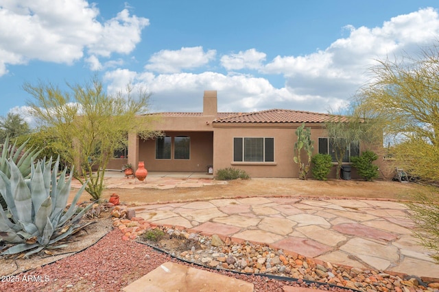 rear view of property with a tile roof, stucco siding, a chimney, and a patio