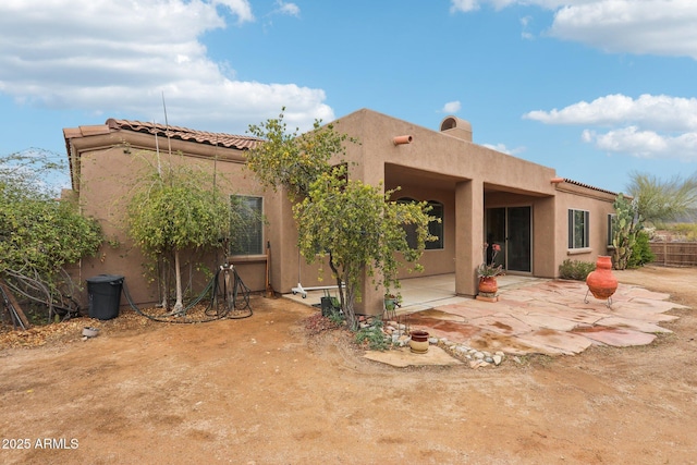 rear view of property featuring a patio area, stucco siding, a tiled roof, and a chimney