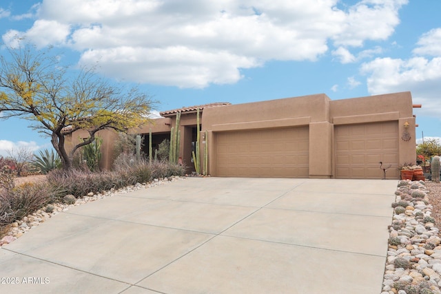 pueblo-style house featuring a tiled roof, a garage, driveway, and stucco siding