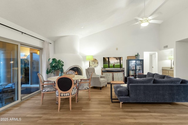 living room with visible vents, ceiling fan, high vaulted ceiling, light wood-type flooring, and a lit fireplace