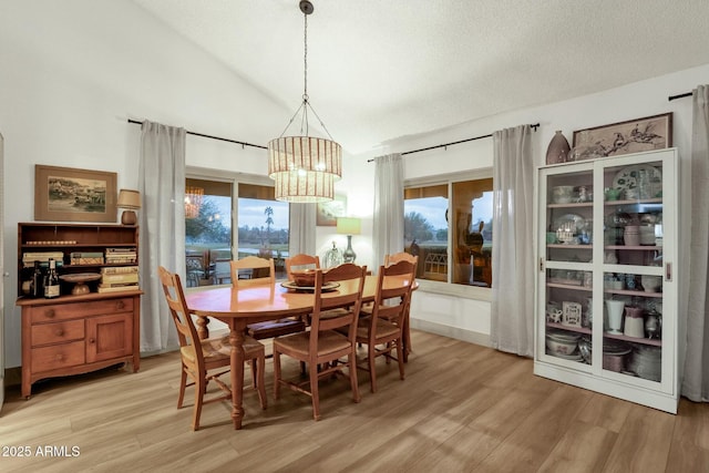 dining space featuring lofted ceiling, light wood-style floors, a textured ceiling, and an inviting chandelier