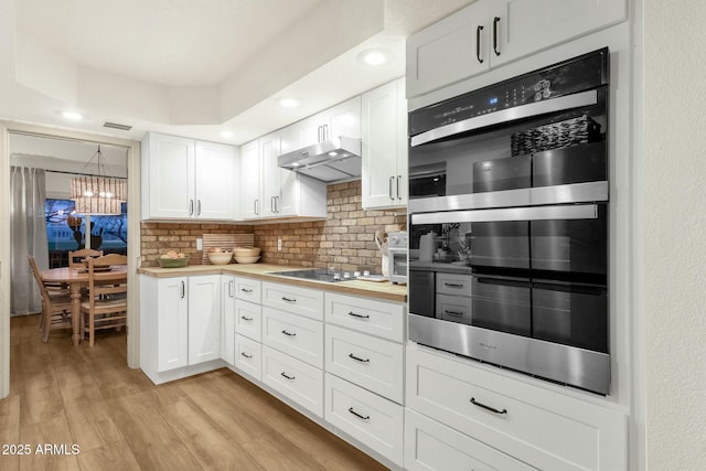 kitchen featuring light wood finished floors, backsplash, double oven, white cabinetry, and under cabinet range hood