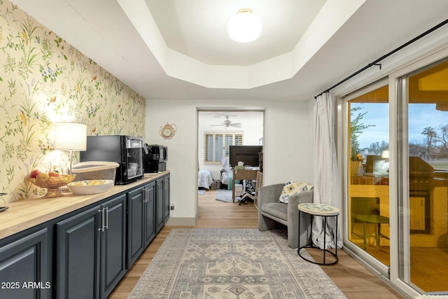 kitchen featuring a tray ceiling, an accent wall, light wood-style floors, baseboards, and wallpapered walls