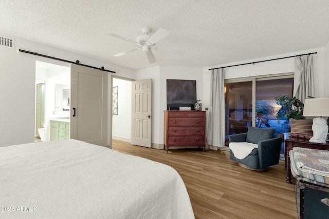 bedroom with a barn door, a ceiling fan, wood finished floors, access to outside, and a textured ceiling