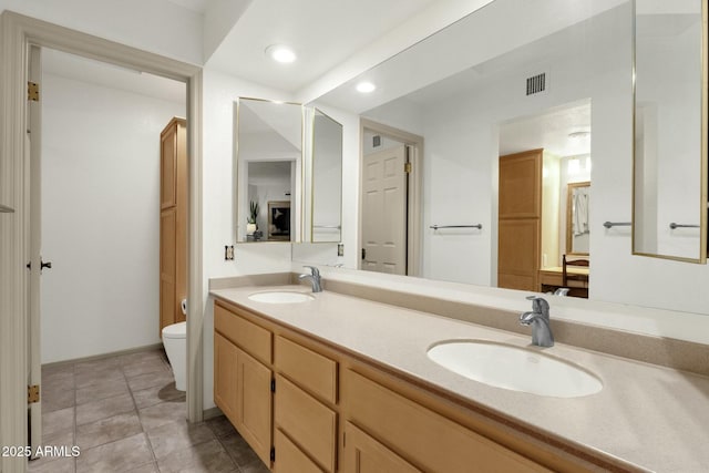 full bathroom with toilet, double vanity, visible vents, and a sink