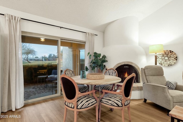 dining area with light wood-type flooring, a warm lit fireplace, vaulted ceiling, and a textured ceiling