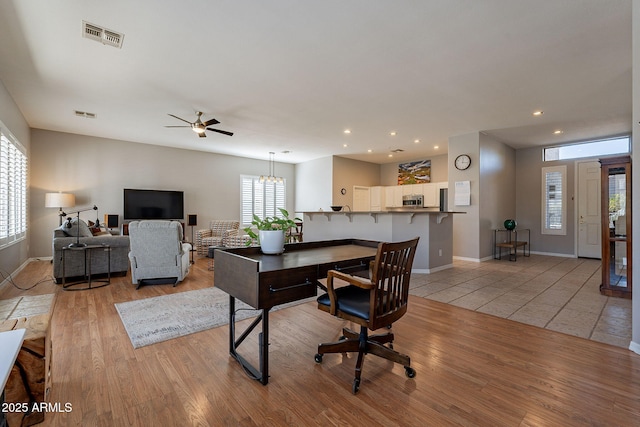 office area with ceiling fan with notable chandelier and light wood-type flooring