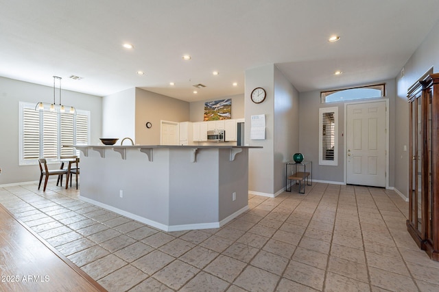 kitchen featuring white cabinetry, kitchen peninsula, decorative light fixtures, a breakfast bar, and light tile patterned flooring