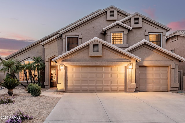 traditional-style house featuring an attached garage, driveway, a tile roof, and stucco siding