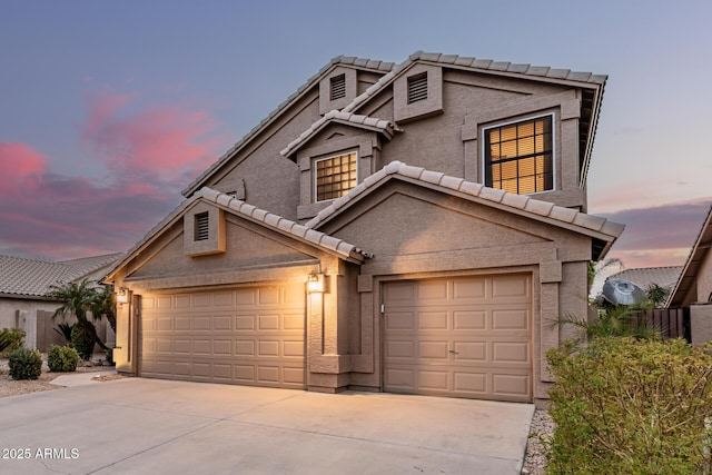 traditional-style home with concrete driveway, a tiled roof, an attached garage, and stucco siding