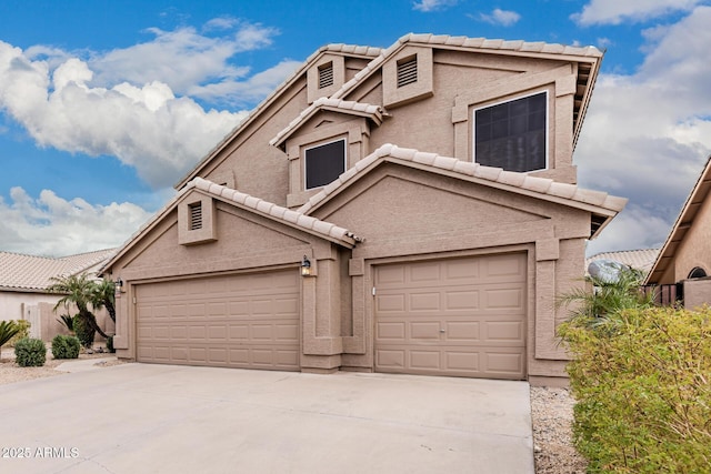 traditional-style house with a garage, driveway, a tiled roof, and stucco siding