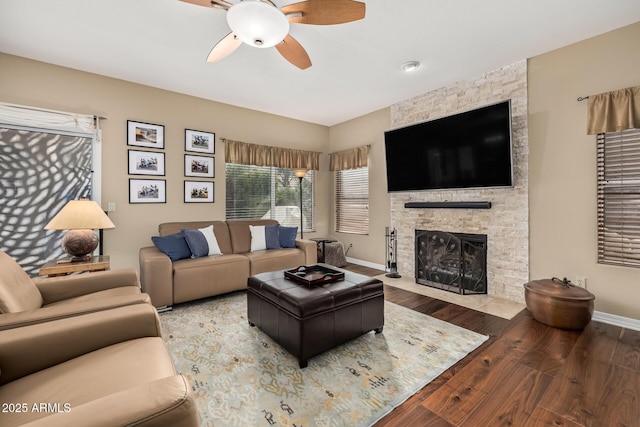 living area with a stone fireplace, wood finished floors, a ceiling fan, and baseboards