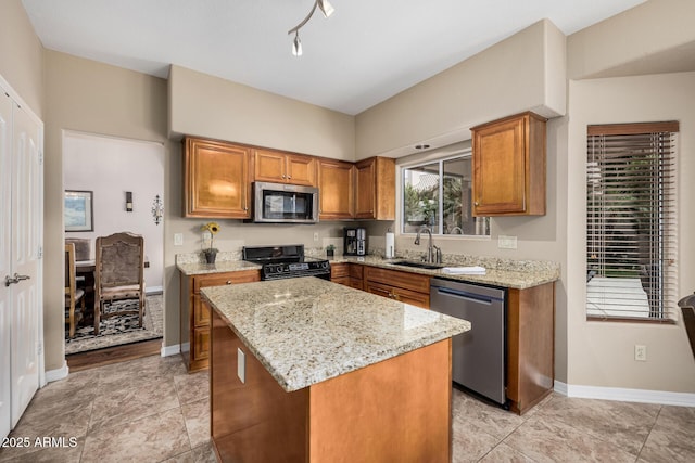 kitchen with light stone counters, a kitchen island, a sink, appliances with stainless steel finishes, and brown cabinetry