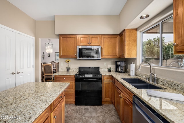 kitchen featuring appliances with stainless steel finishes, brown cabinetry, a sink, and light stone countertops