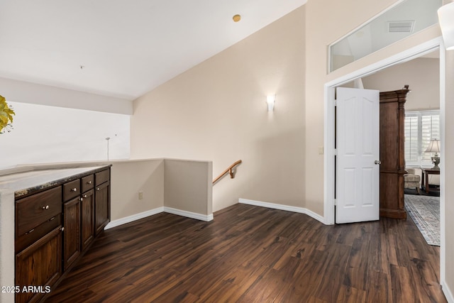 interior space featuring dark wood-type flooring, baseboards, visible vents, and an upstairs landing