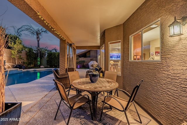 patio terrace at dusk featuring outdoor dining area, fence, and a fenced in pool