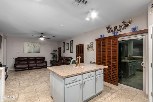 kitchen featuring white cabinetry, ceiling fan, a kitchen island, and light stone counters