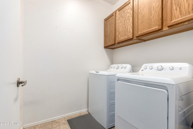 clothes washing area with washer and clothes dryer, light tile patterned floors, and cabinets