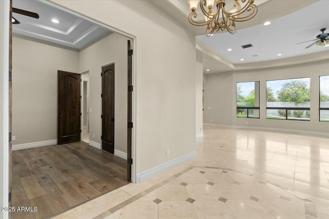 empty room with ceiling fan with notable chandelier and a tray ceiling