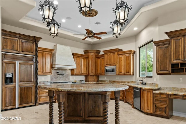 kitchen with premium range hood, built in appliances, a center island, decorative light fixtures, and a tray ceiling