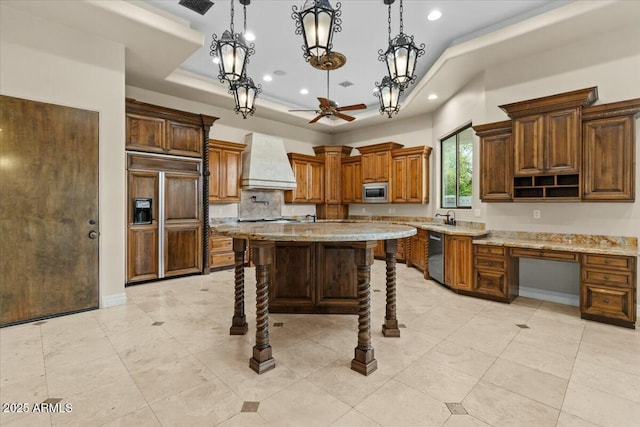 kitchen with built in appliances, hanging light fixtures, a tray ceiling, a kitchen island, and custom range hood