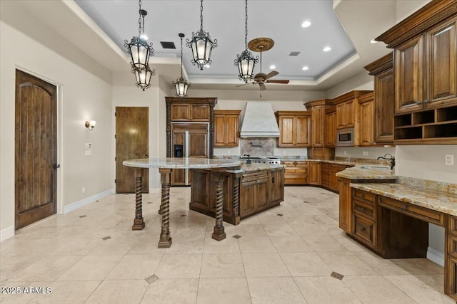 kitchen featuring a center island, built in appliances, custom range hood, decorative light fixtures, and a raised ceiling