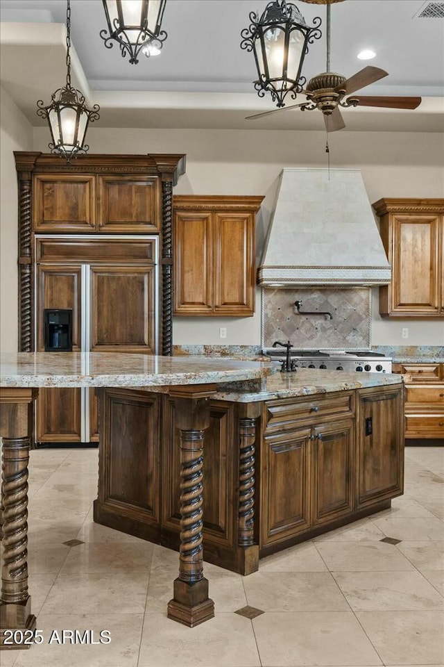 kitchen featuring premium range hood, a kitchen island with sink, light stone countertops, decorative light fixtures, and stainless steel gas stovetop