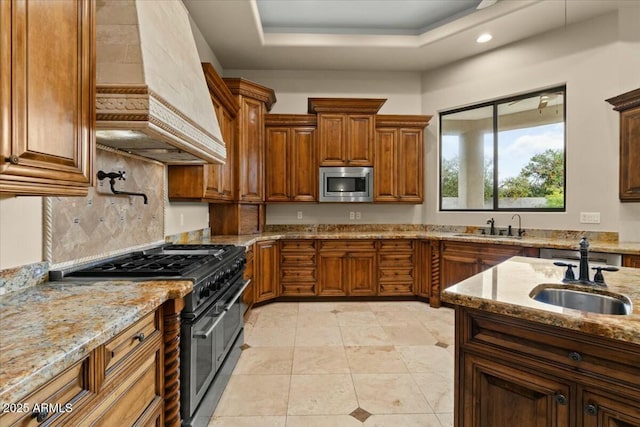 kitchen with stainless steel microwave, sink, custom exhaust hood, double oven range, and a tray ceiling