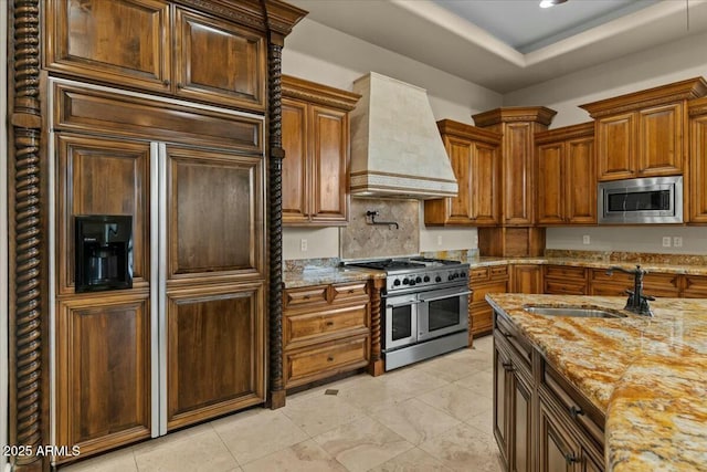 kitchen featuring sink, custom exhaust hood, light stone counters, a raised ceiling, and stainless steel appliances