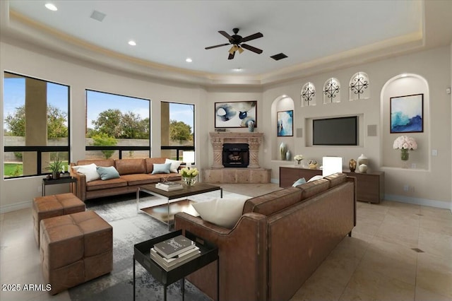 tiled living room featuring ceiling fan, a tray ceiling, and a tiled fireplace