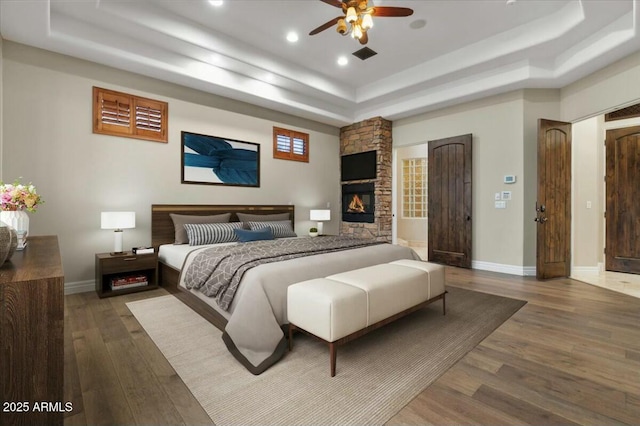 bedroom with ceiling fan, hardwood / wood-style floors, a fireplace, and a tray ceiling