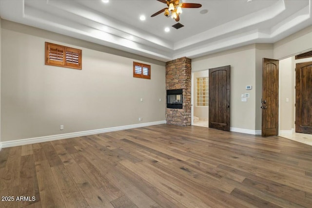 unfurnished living room featuring hardwood / wood-style floors, a tray ceiling, a fireplace, and ceiling fan