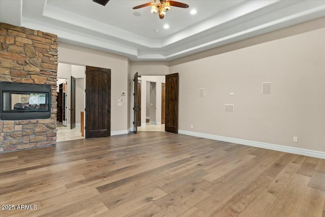 unfurnished living room featuring a fireplace, a tray ceiling, and light wood-type flooring